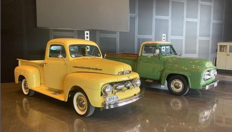 a yellow and green classic car parked inside a high ceiling garage with a polished concrete floor