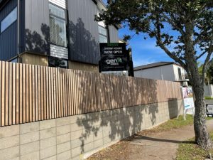 wooden pailing fence with retaining wall under made of honed concrete blocks in dappled shade of a tree on the footpath and a house behind the fence