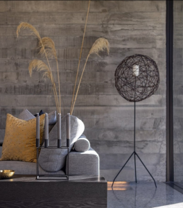 NZ Architecture polished concrete floors image of a polished concrete floor in loumnge area with a safa and floor lamp in background. Pampas grass is in a vase behind tje sofa and candles are on the coffee table in a candlestick holder