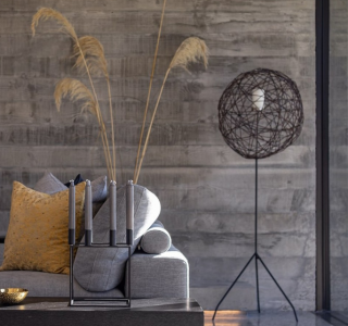 NZ Architecture polished concrete floors image of a polished concrete floor in loumnge area with a safa and floor lamp in background. Pampas grass is in a vase behind tje sofa and candles are on the coffee table in a candlestick holder