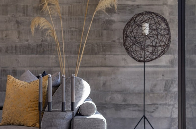 NZ Architecture polished concrete floors image of a polished concrete floor in loumnge area with a safa and floor lamp in background. Pampas grass is in a vase behind tje sofa and candles are on the coffee table in a candlestick holder