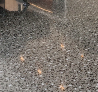 Close up image of a diamond polished concrete floor with full stone exposure and a leg of a sofa in the background