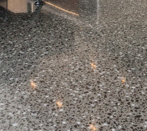 Close up image of a diamond polished concrete floor with full stone exposure and a leg of a sofa in the background