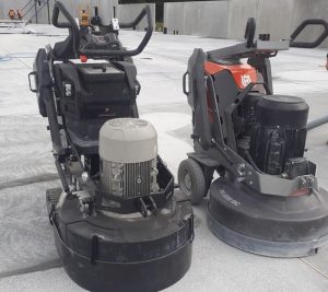 close up image of 2 concrete grinding machines side by side on a part finished concrete floor