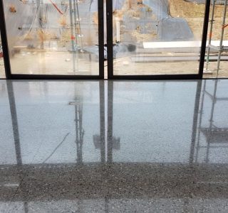 NZ Grinders Tauranga Polished concrete floor in front of large windows house under construction with planting of garden on slope in background