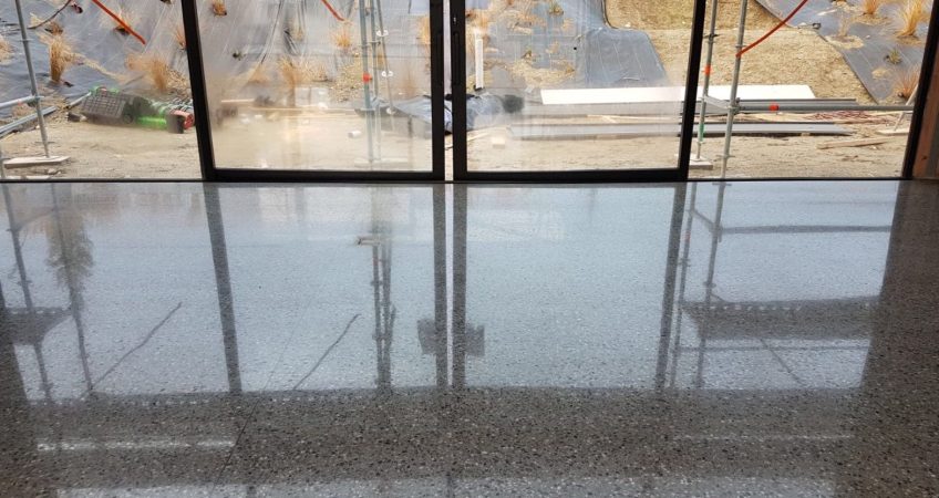 NZ Grinders Tauranga Polished concrete floor in front of large windows house under construction with planting of garden on slope in background